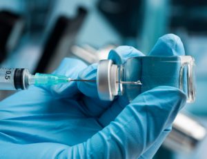 mão com luva cirurgica azul insere uma injeção com agulha em frasco com léquido transparente